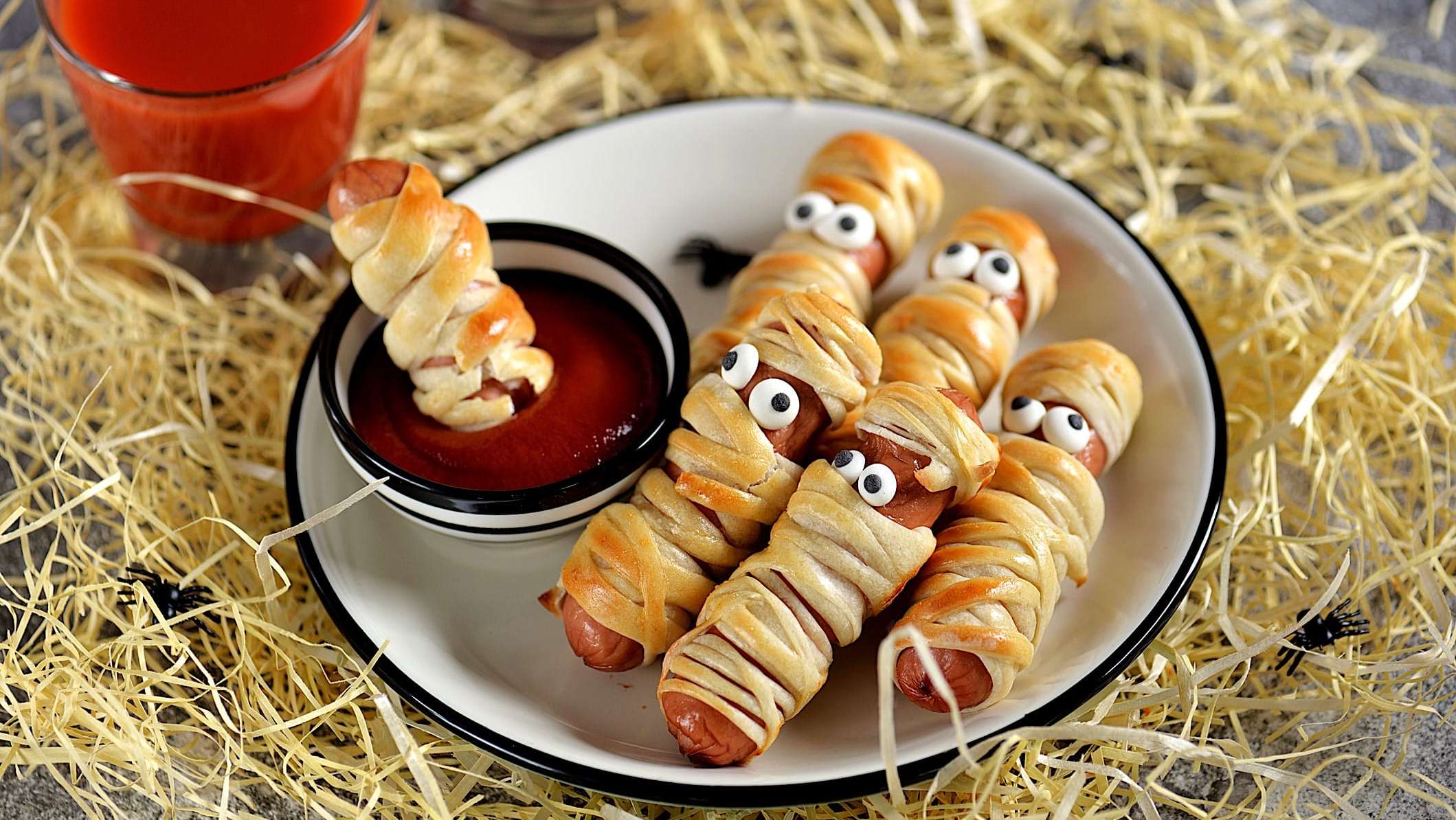 Une assiette blanche contient des saucisses-momies, enroulées dans des bandelettes de pâte et décorés avec des yeux faits de fromage et olive noire pour une boite à lunch de l'Halloween
