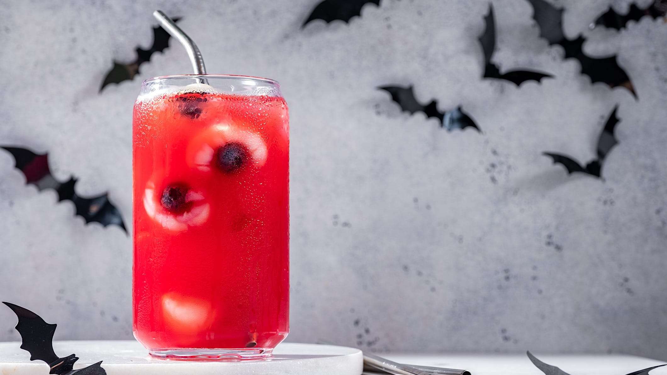 boite-lunch-halloween-yeux-jus Sur un fond de décor d'halloween de chauves-souris, un verre de jus est décoré avec des yeux globuleux faits à partir de litchis et de bleuets pour une boîte à lunch de l'Halloween