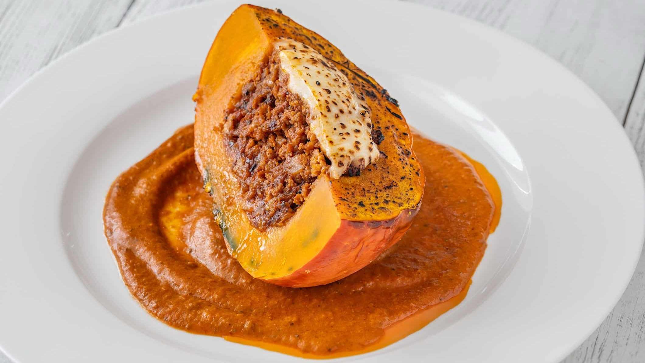 recettes-viande-citrouille_farcie Un quartier de citrouille farci à la viande hachée et gratiné est posé sur un lit de sauce tomate dans une assiette ronde blanche