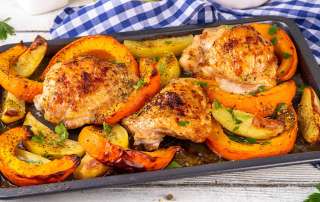 Une plaque de cuisson au four est remplie de cuisses de poulet rôties au four avec des tranches de citrouilles et des quartiers de pommes de terre