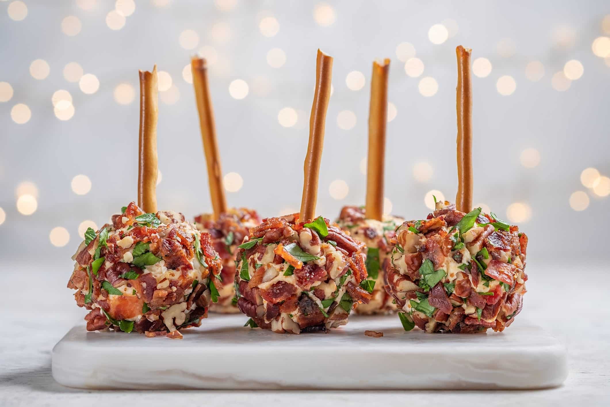Bouchees-potluck-temps-des-fetes-boules-fromage-bacon-pacanes Des minis boules de fromages au bacon et pacanes avec un pretzel en batonnêt pour illustrer une recette de bouchées du temps des fêtes à amener à un potluck