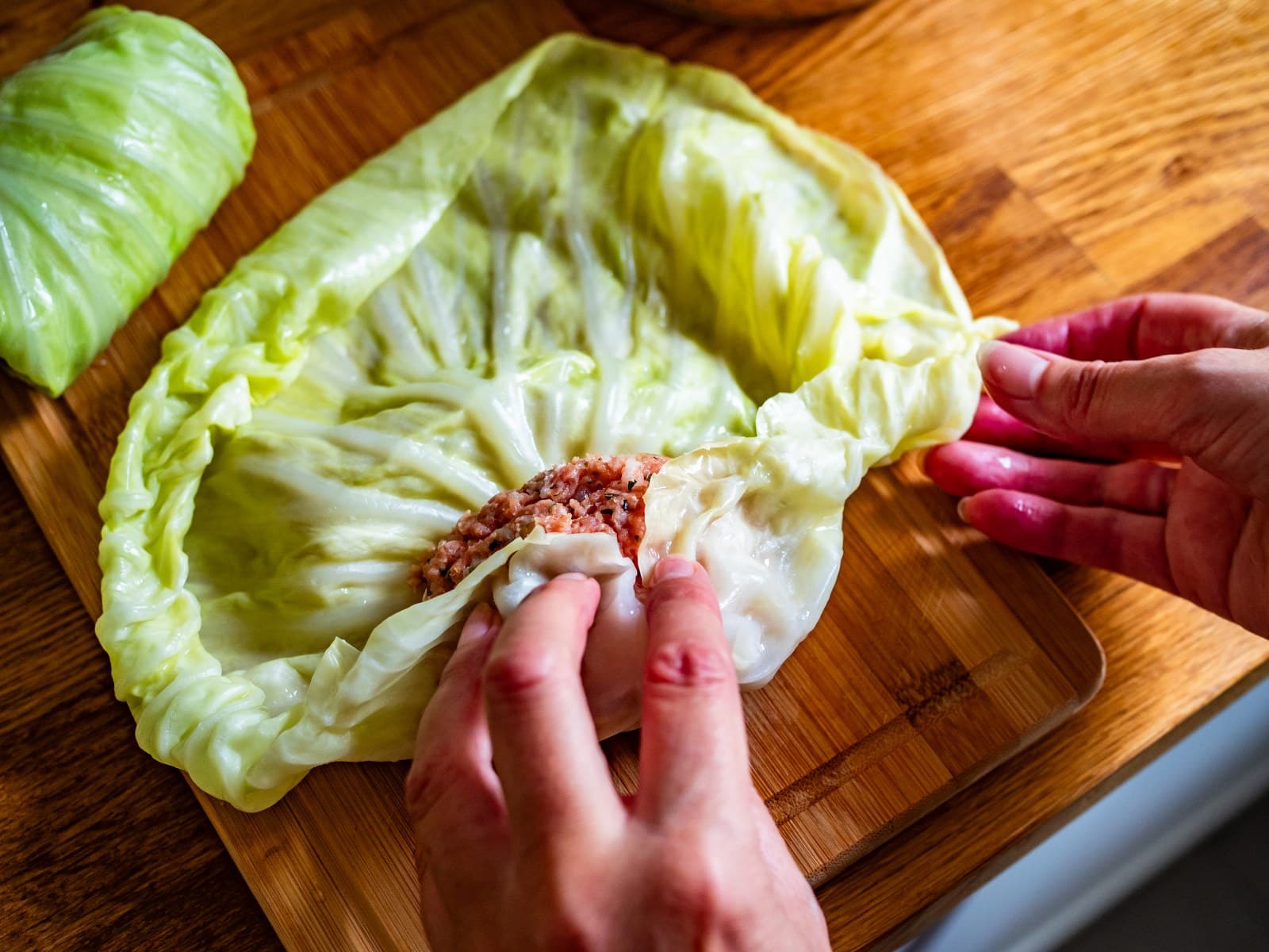 Recettes-cigares-au-chou-rouler.jpeg Les mains d'une femme roulent la farce d'une recette de cigares au chou dans une feuille de chou vert blanchie.