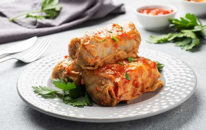 Trois cigares au chou sont dressés dans une assiette blanche et garnies de persil.