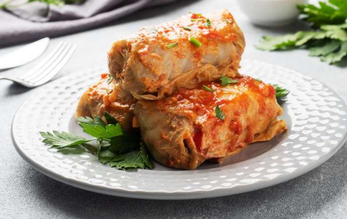 Trois cigares au chou sont dressés dans une assiette blanche et garnies de persil.