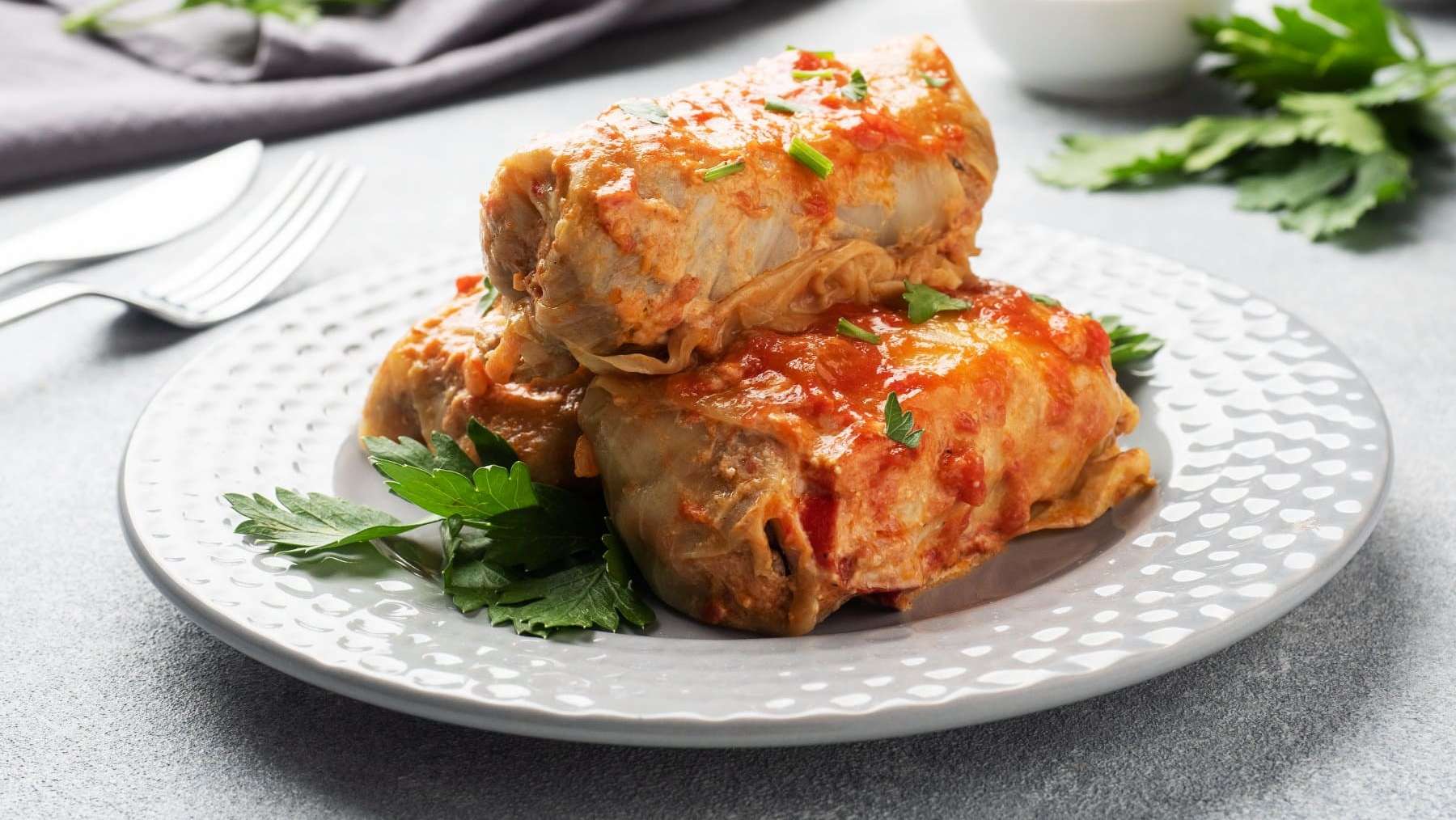 Trois cigares au chou sont dressés dans une assiette blanche et garnies de persil.