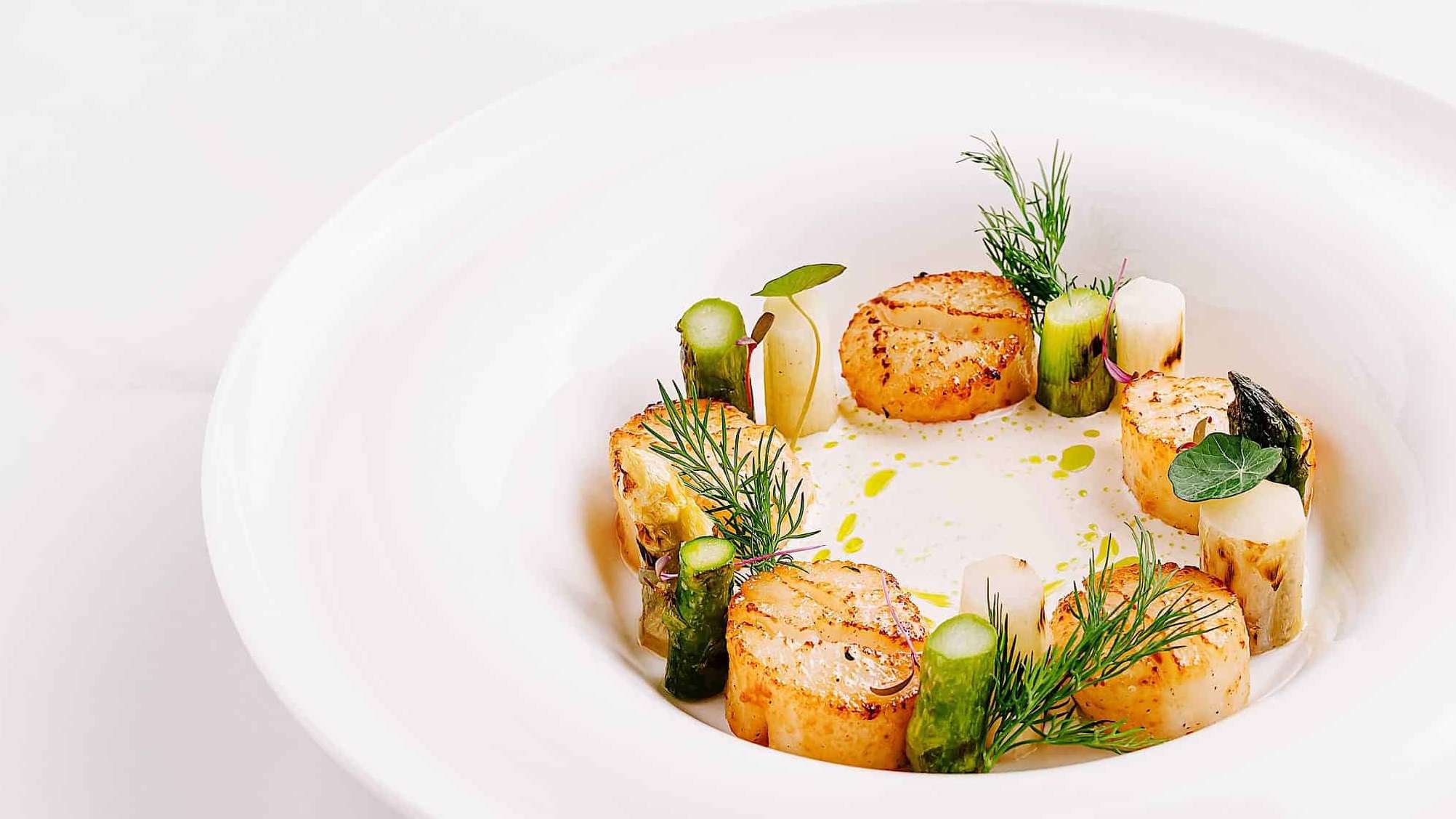 Des pétoncles poêlées sont dressées dans une assiette blanche pour illustrer des idées de repas pour remplacer la classique dinde de Noël.