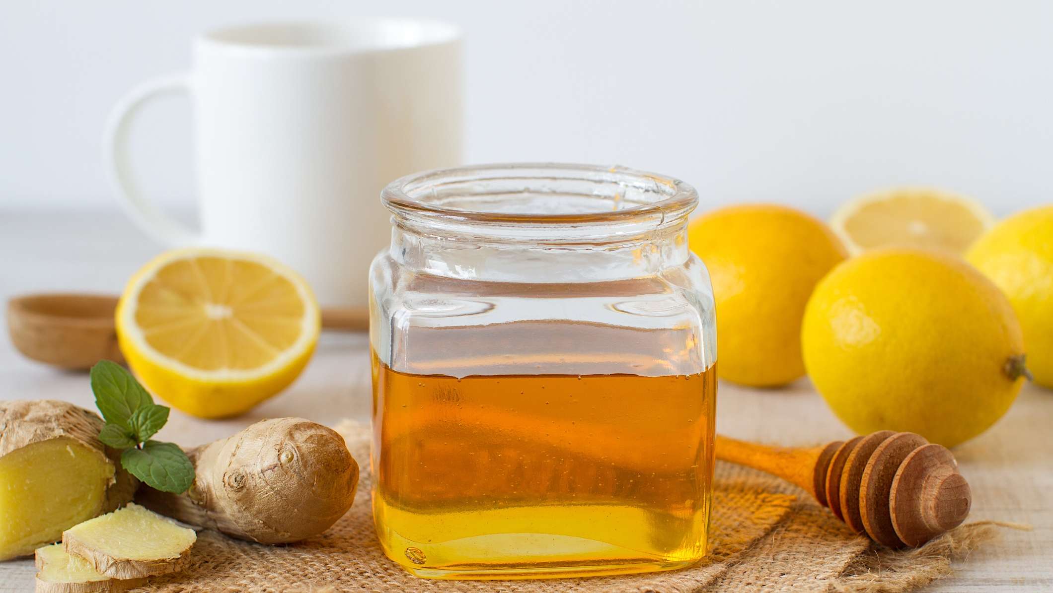 quoi-manger-boire-rhume-grippe_miel-gingembre-citron Un pot de miel accompagné de morceaux de racine de gingembre, de citron frais et de menthe pour illustrer quoi manger et quoi boire pour pour soigner un rhume ou une grippe