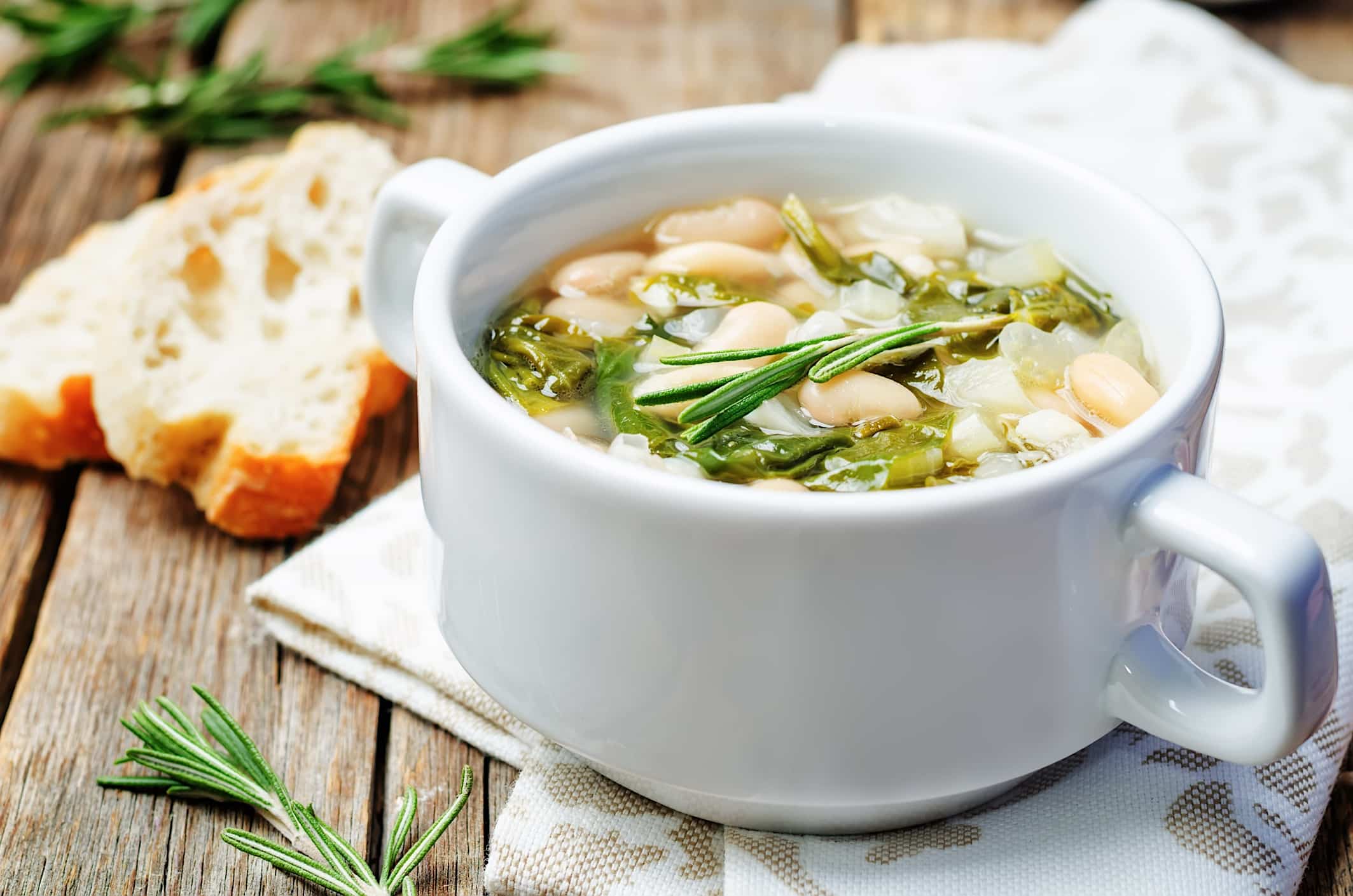 Un bol de service blanc contient une recette de soupe aux épinards et haricots blancs cuisinée avec des légumes surgelés