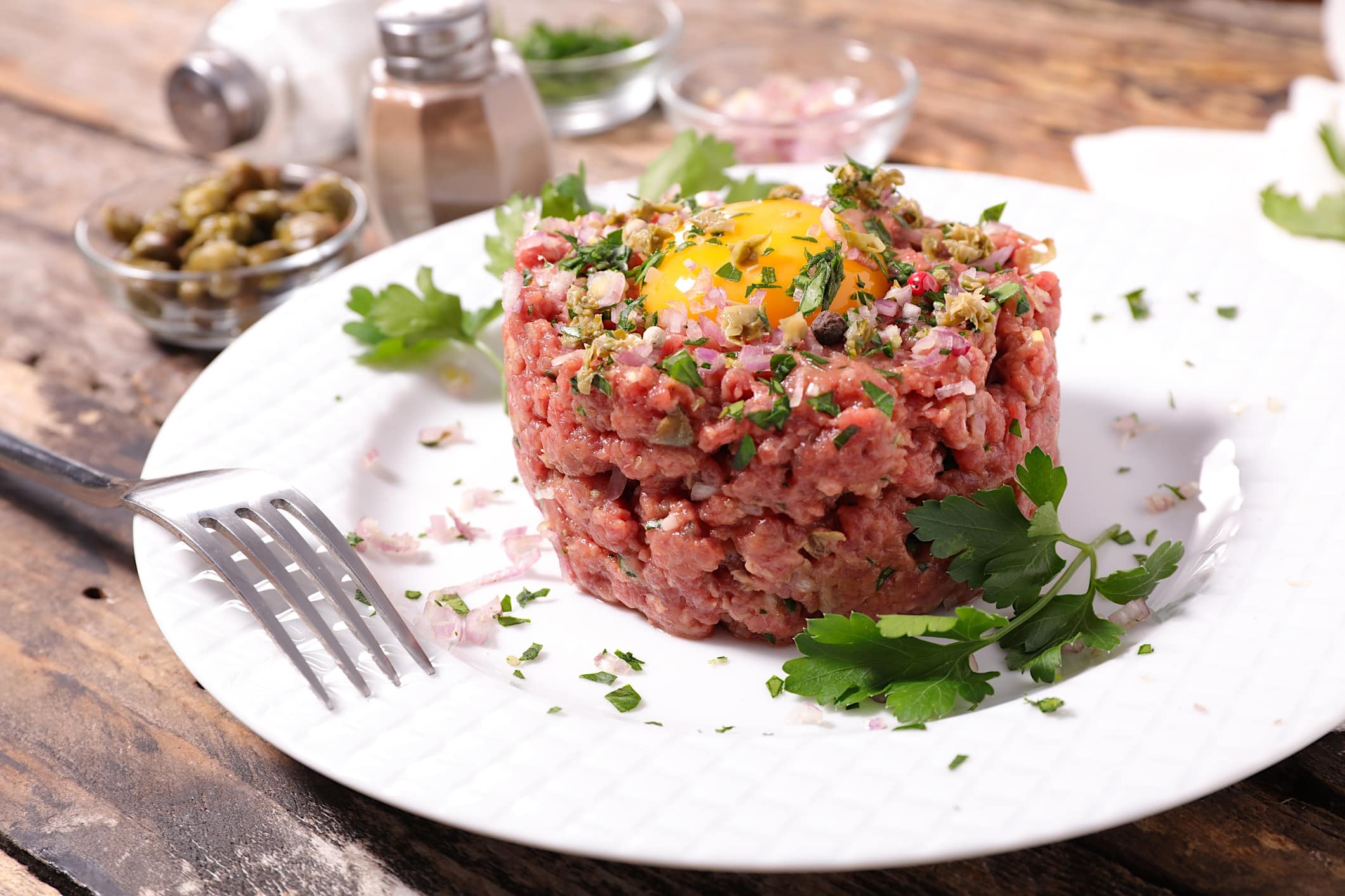 Une recette de tartare de boeuf classique dressé dans une assiette blanche et garni d'un jaune d'oeuf posé sur le dessus.