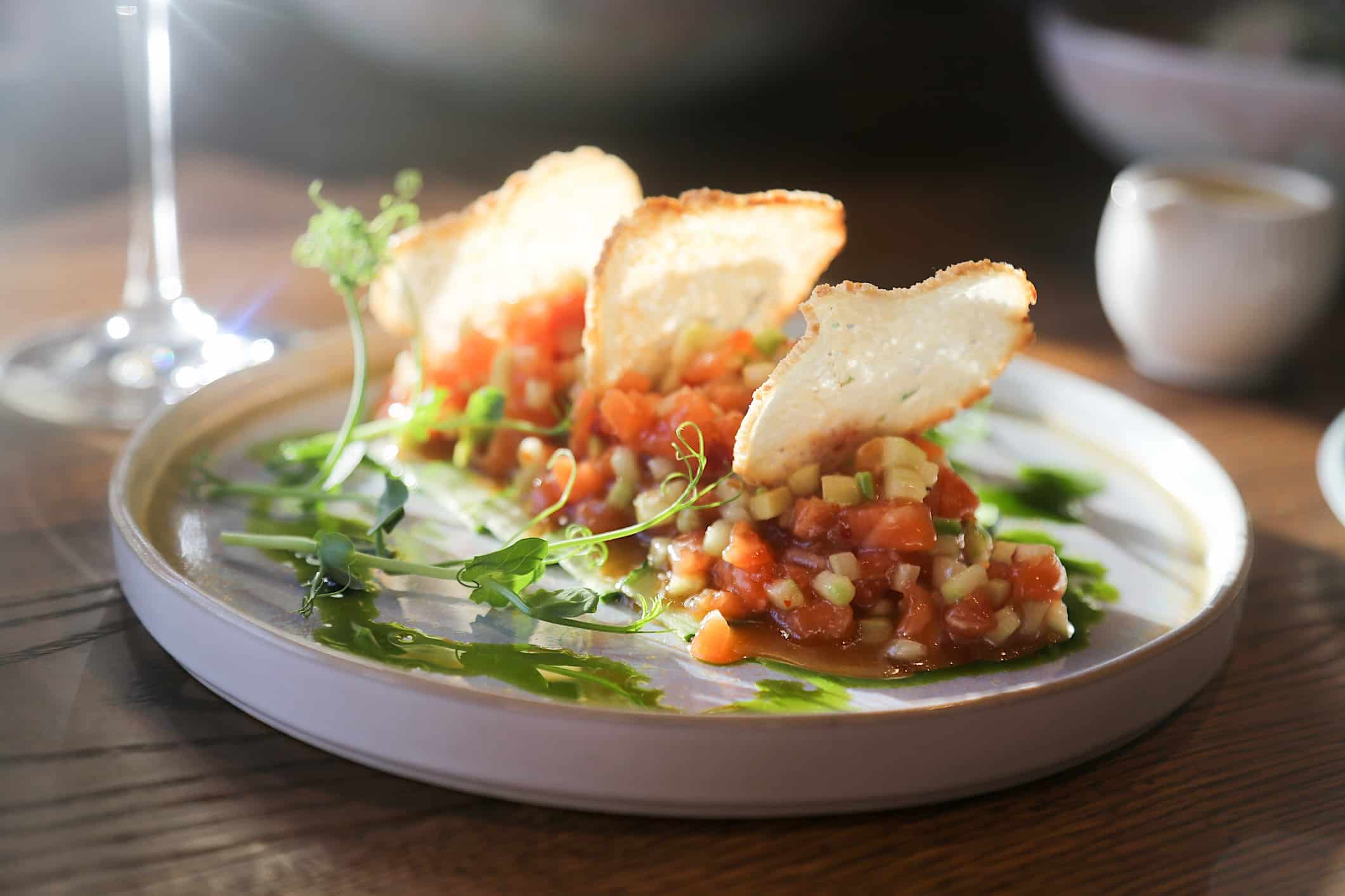 Une recette de tartare de saumon est dressé dans une assiette et accompagné de craquelins de pain baguette