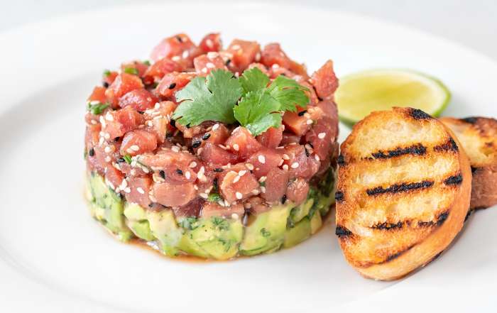 Une recette de tartare de thon à l'avocat est dressé dans une assiette et accompagné de croutons de pain