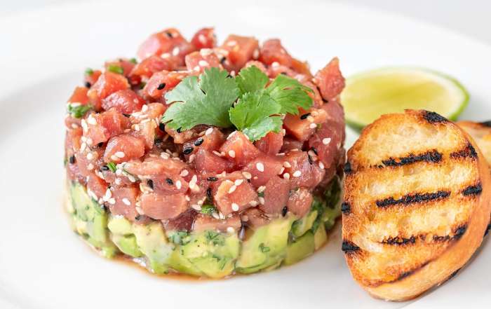 Une recette de tartare de thon à l'avocat est dressé dans une assiette et accompagné de croutons de pain