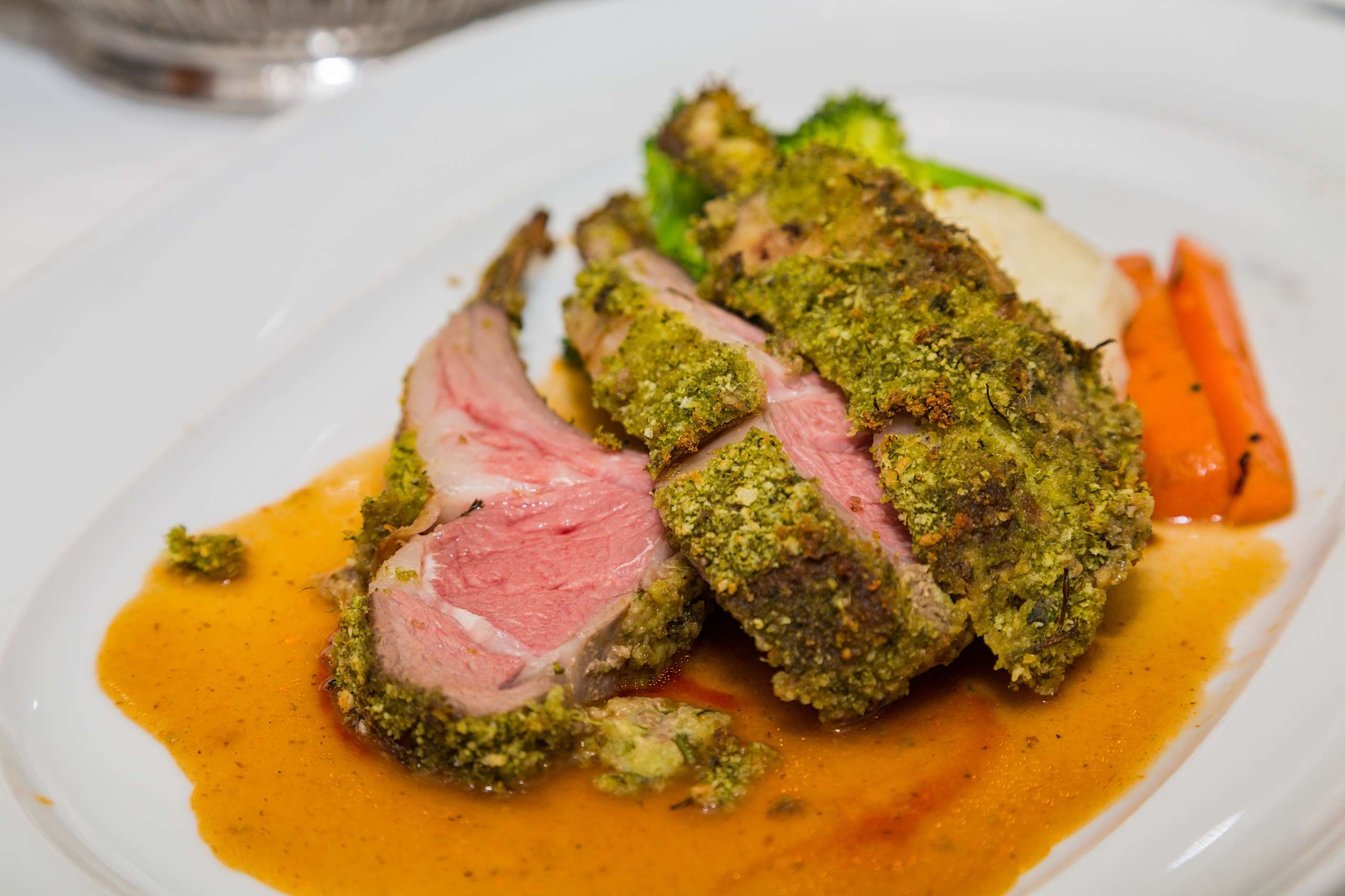 3 côtelettes de porc avec une croûte à la pistache et aux herbes sont dressée dans une assiette avec des légumes et une sauce pour illustrer une recette de viande pour un menu de Pâques sans jambon