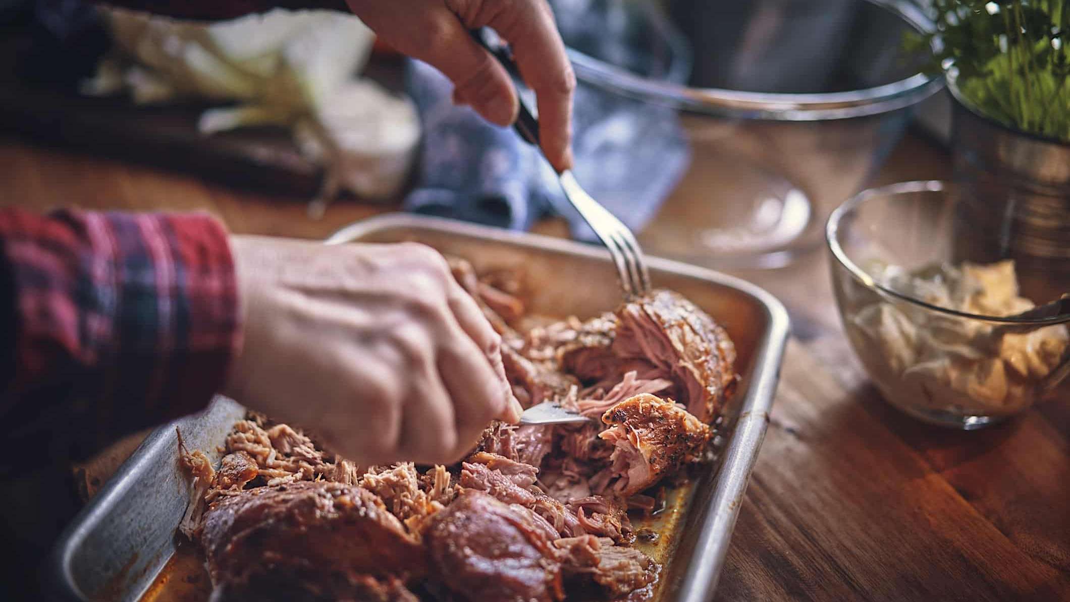 Une personne effiloche avec 2 fourchettes une recette de cretons d'épaule de porc au gras de canard