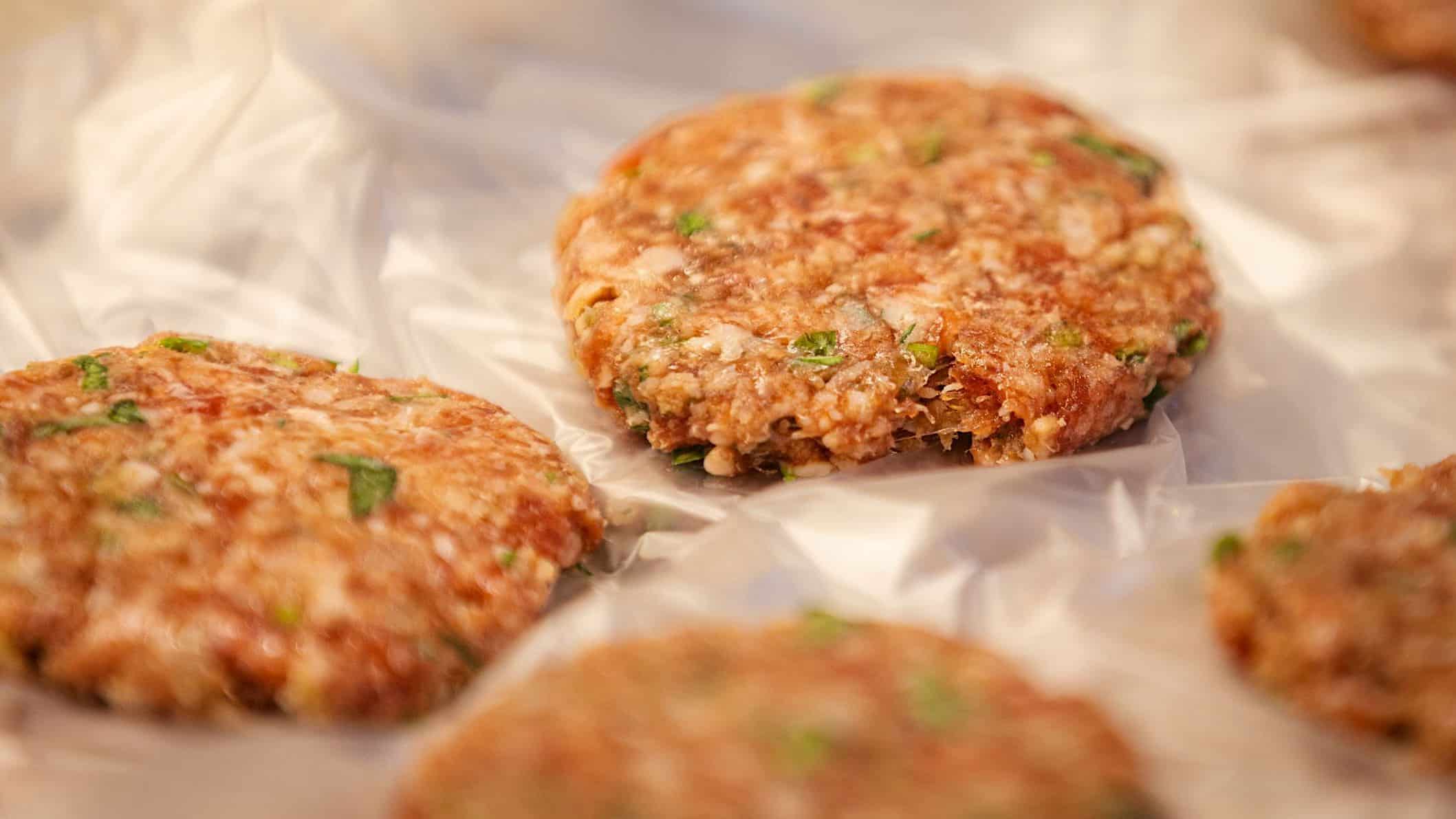 Des galettes de chair à saucisses déjeuner posés sur du papier parchemin cuisinés à partir d'une recette de petit déjeuner au sirop d'érable.