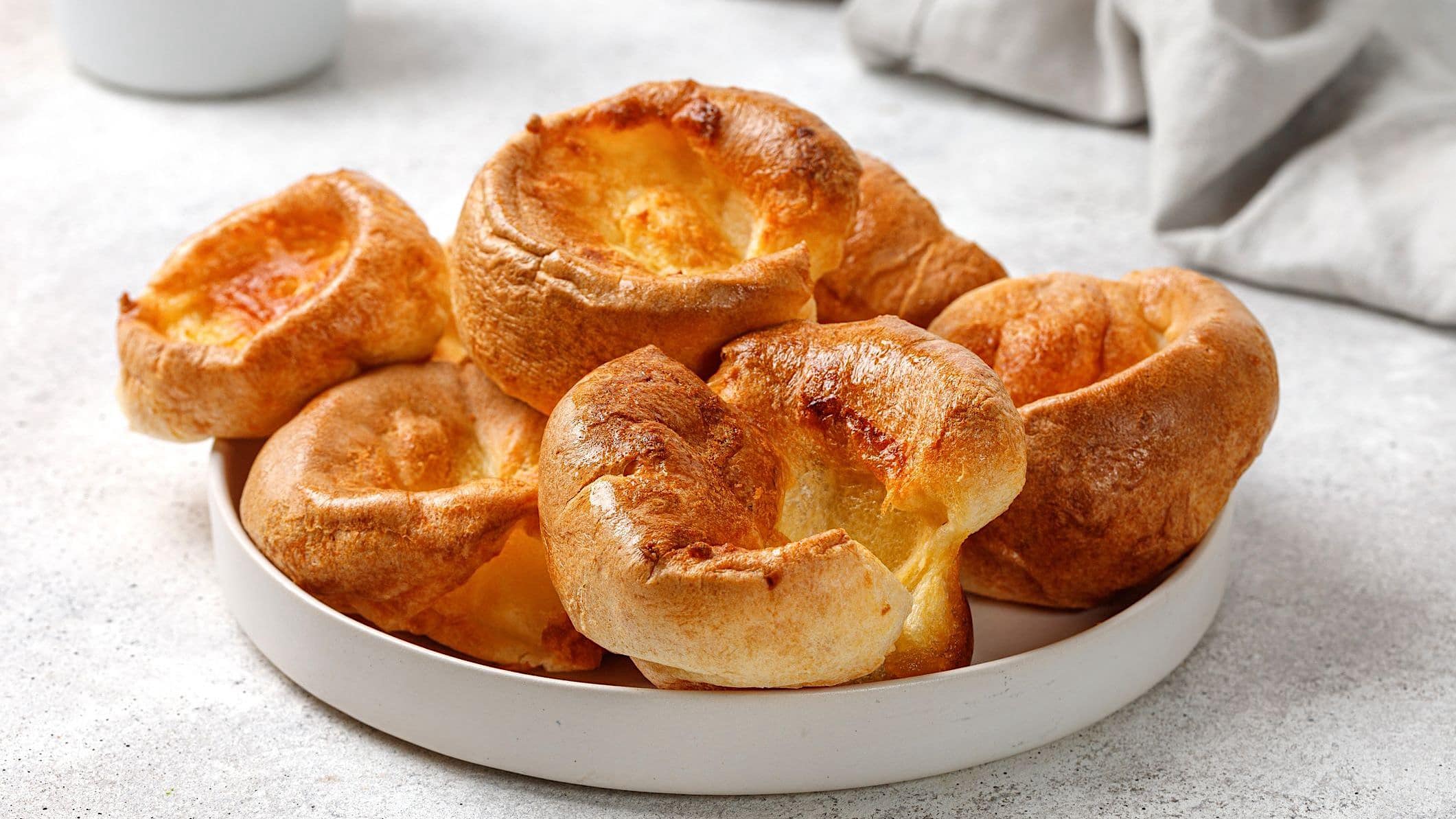 Une assiette blanche contient des popovers cuisinés avec une recette de petit déjeuner au sirop d'érable et bacon.