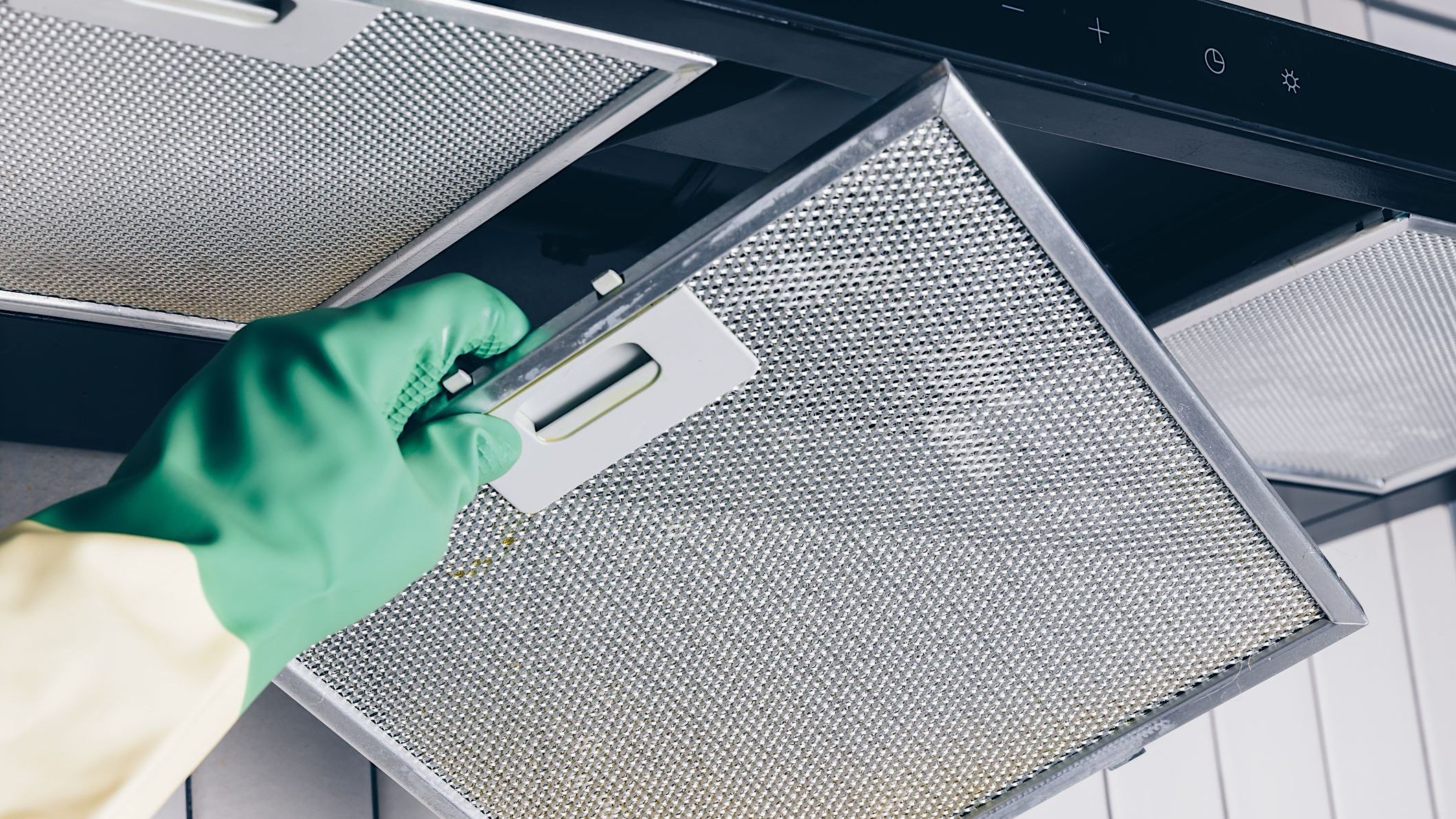 Gros plan d'une main gantée qui retire une grille de hotte de cuisinière afin d'illustrer comment faire le grand ménage du printemps de la cuisine.