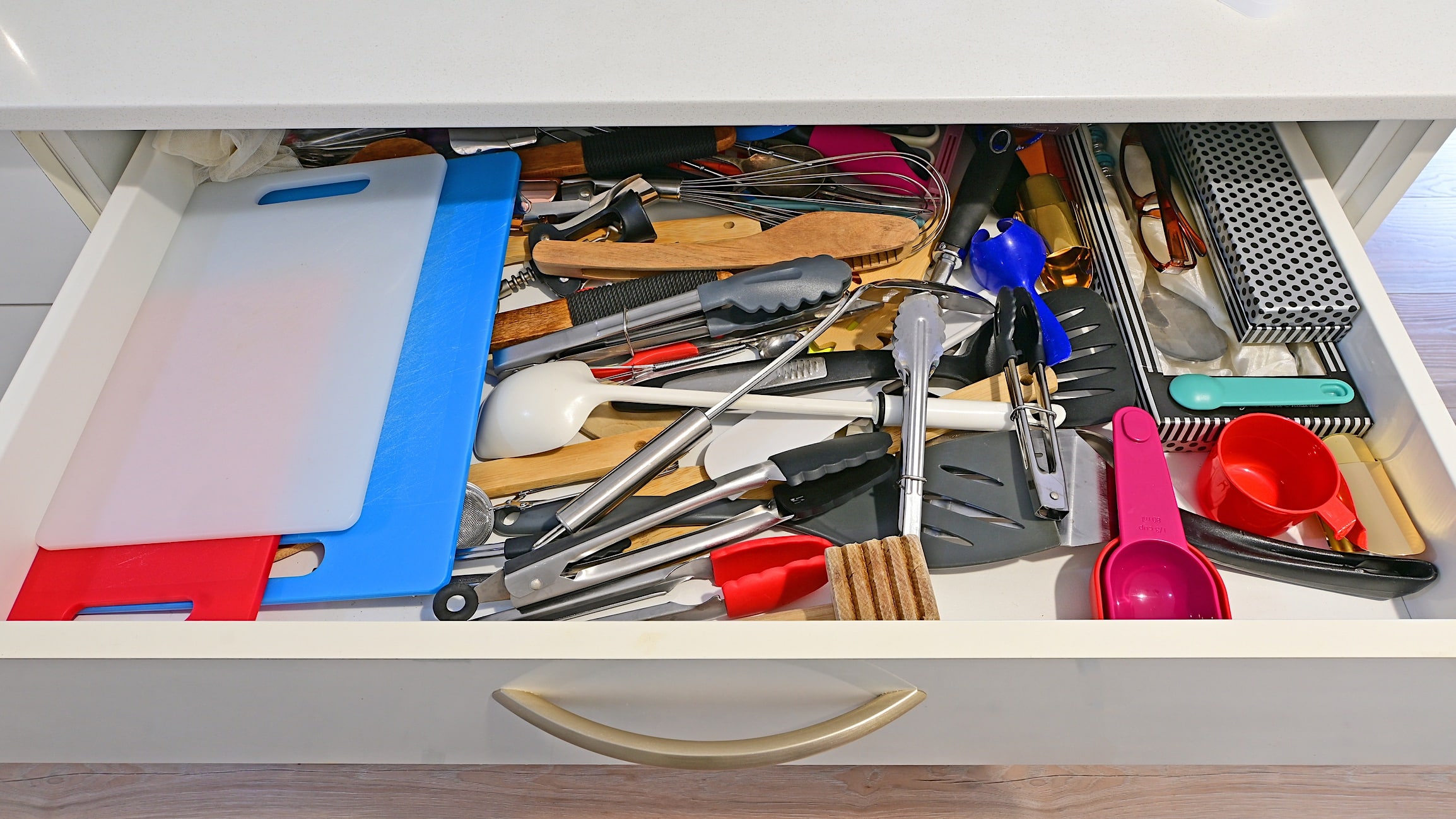 Un grand tiroir de cuisine contient pleins d'outils et d'ustensiles de cuisine pêles-mêles pour illustrer comment faire le grand ménage du printemps de la cuisine.