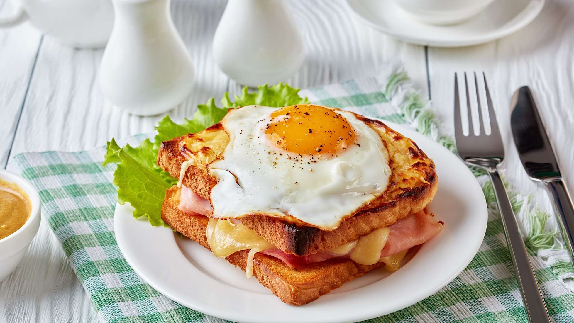 recettes-restes-jambon-paques-croque-madame Une assiette blanche posée sur un linge à carreaux vert contient un croque-madame cuisiné avec des restes de jambon de Pâques